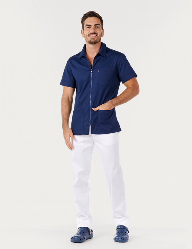 Homme avec blouse médicale bleu marine à manches courtes et col chemise. Pantalon blanc. Marque Belissa Medical style