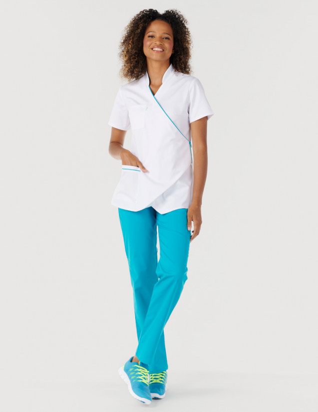 Femme avec blouse médicale blanc et bleu océan à manches courtes, coupe asymétrique + pantalon bleu océan. Marque Belissa